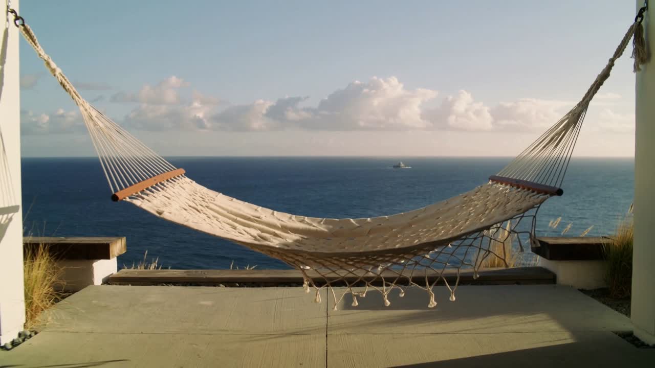 Amaca color crema ondeggiante che reagisce a una folata di vento da terra, oscillando e poi stabilizzandosi su una terrazza a picco sulla scogliera.