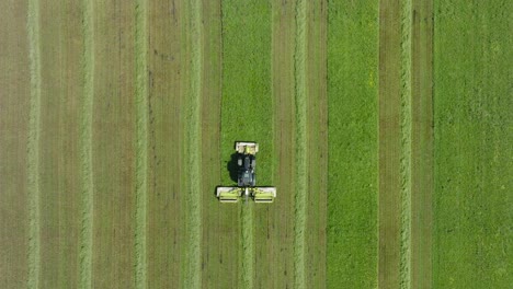 aerial establishing view of a tractor mowing a fresh green grass field, a farmer in a modern tractor preparing food for farm animals, sunny summer day, wide birdseye drone shot moving forward
