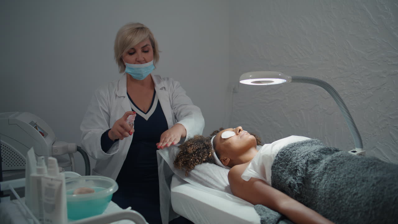 Médico aplica antisséptico na pele em salão. Esteticista pulverizando líquido antibacteriano.