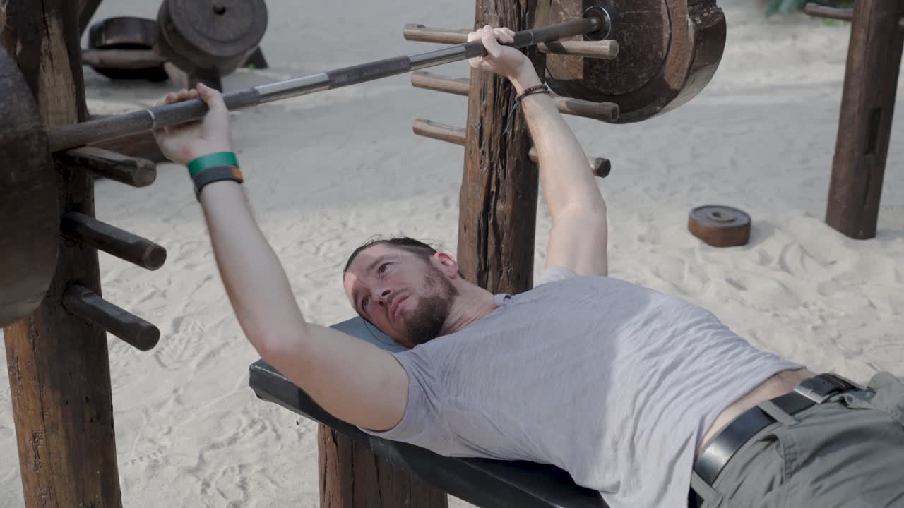 A man lifts weights on the sandy shores of Koh Phangan, Thailand, blending fitness and beach vibes. The power of strength training amidst nature’s beauty creates the ultimate workout experience.