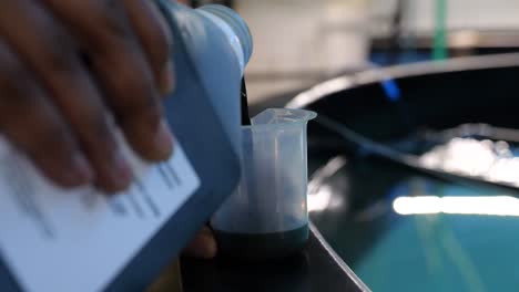 a person pours a dark green colored nutrient mix into a plastic measuring  jug