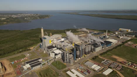 aerial view of paper mill factory with smoky chimneys in front to river in fray bentos,uruguay - environmental pollution of earth