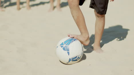 Vertical-motion-of-boy-standing-on-beach-with-leg-on-soccer-ball