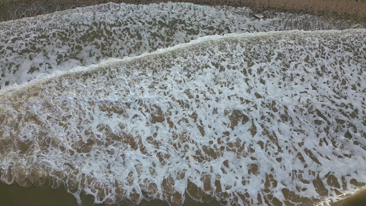Whitecaps breaking from murky brown sea onto shallow pebbled beach
