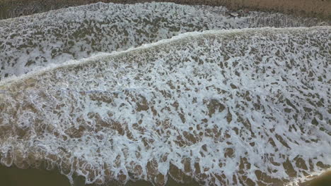 whitecaps breaking from murky brown sea onto shallow pebbled beach