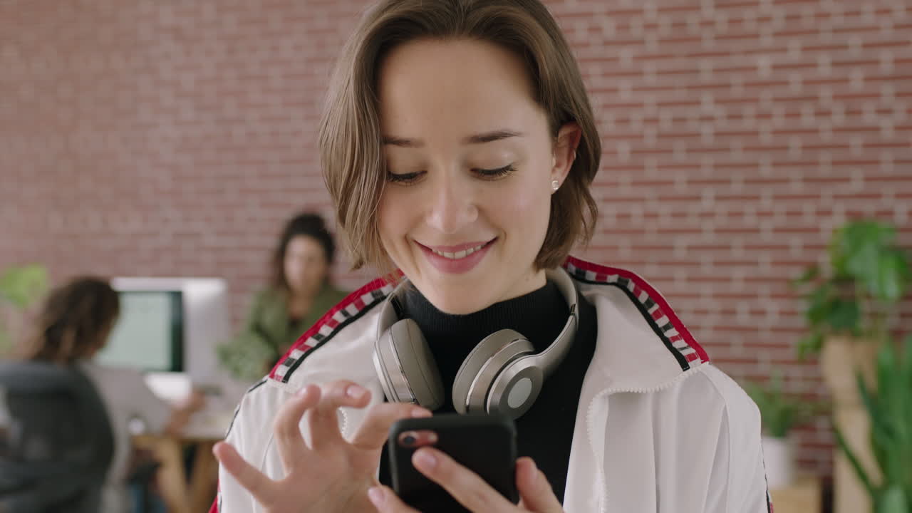 retrato de una joven caucásica elegante sonriendo, enviando mensajes de texto relajados, navegando usando una aplicación de redes sociales para teléfonos inteligentes en un espacio de trabajo de oficina moderno.