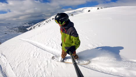 man in protective helmet, green and grey blazer and brown pants rides on the snowboard. fantastic snowy landscape at backdrop.