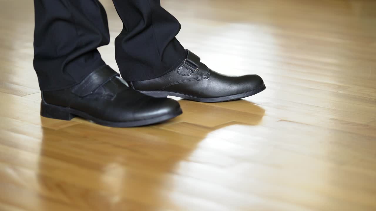 Man's legs shows black shoes standing on heels and goes away on the wooden floor. Legs of a young man in the dancing shoes. Close-up
