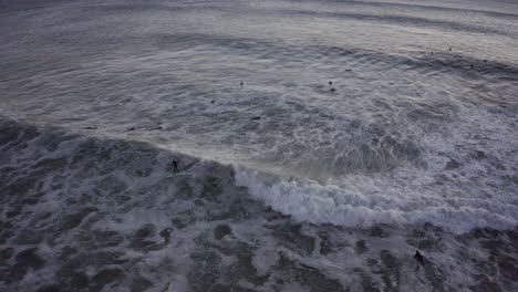 Surfer-drops-in-on-a-huge-wave-in-slow-motion-in-the-moody-dark-cold-water-evening-light-in-estoril,-cascais