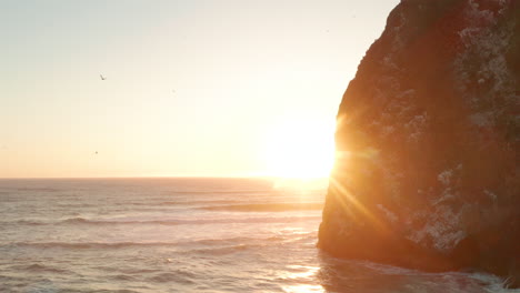 aerial slider shot past large sea cliffs revealing the sunset