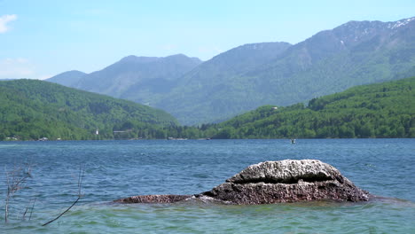 Water-peacefully-splashing-at-a-rock-in-Lake-Bohinj-with-beautiful-mountain-range-in-background