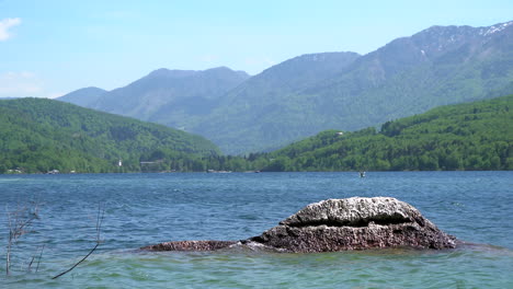 Agua-Salpicando-Pacíficamente-En-Una-Roca-En-El-Lago-Bohinj-Con-Una-Hermosa-Cordillera-En-El-Fondo