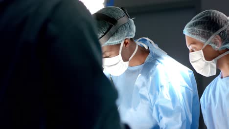 Diverse-surgeons-wearing-surgical-gowns-operating-on-patient-in-operating-theatre,-slow-motion