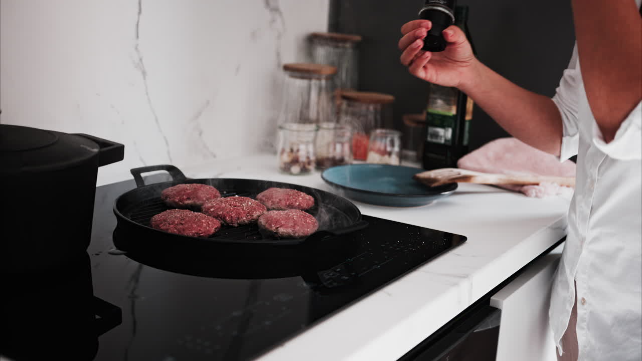 Woman seasoning burger patties being cooked on a grill pan