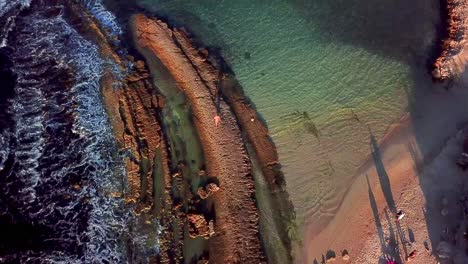 Tilt-up-aerial-view-of-Kanoa-Beach,-family-on-the-shore-enjoying-the-sunset,-Curacao,-Dutch-Caribbean-island