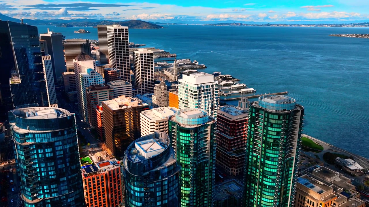 Vista aérea das torres da orla do centro de São Francisco e da Baía de São Francisco. Imagem elevada de drone de arranha-céus de vidro azul-esverdeado, cais de ferry e baía azul profunda com as colinas de Marin sob o céu diurno.