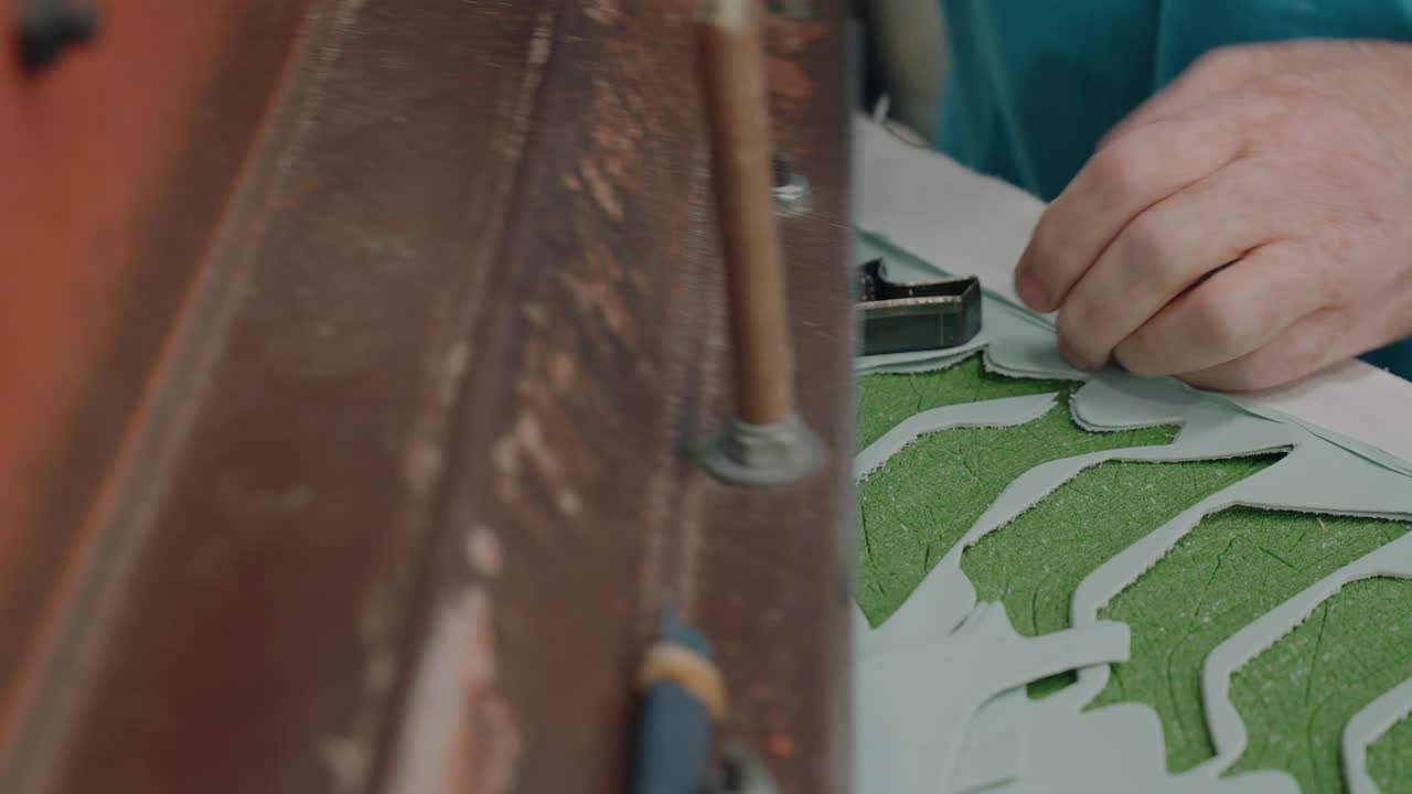 Manos presionando un troquel para cortar piezas de cuero verde en una fábrica de calzado