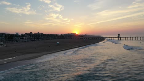 Stunning-4k-view-of-the-sunrise-through-the-pier-as-surfers-catch-a-wave-in-Surf-City-USA-California