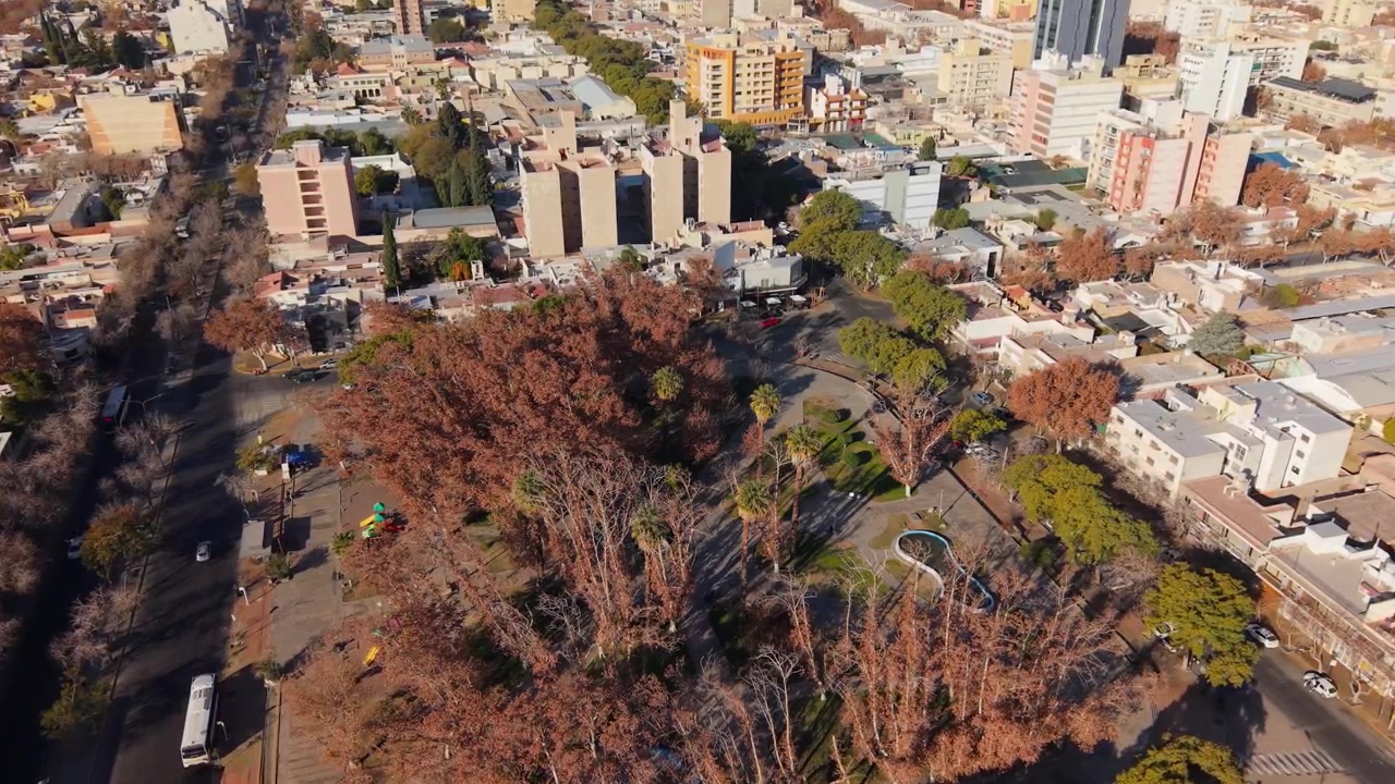 Un video con drone riprende Plaza Laprida, San Juan, Argentina dall'alto, rivelando un vivido fogliame autunnale, il paesaggio urbano, le ombre e una variegata architettura urbana nella nitida luce del mattino.