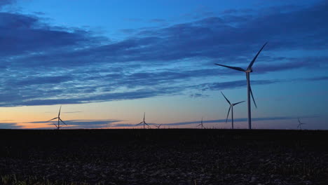 wind turbines at a eolic power plant, colorful dusk sky background with clouds