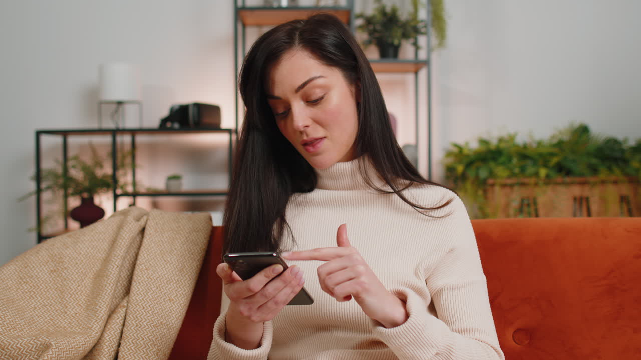 joven mujer morena sentada en el sofá usando un teléfono inteligente compartiendo mensajes en la aplicación de redes sociales