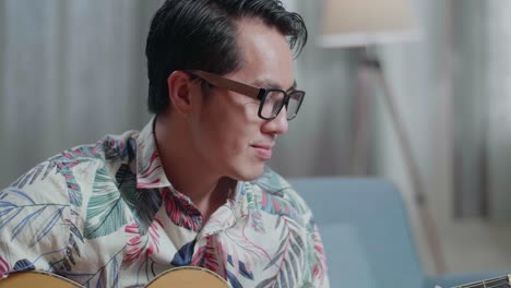 primer plano de un compositor asiático con un cuaderno en la mesa tocando la guitarra en casa