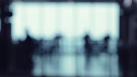 a defocused shot of many silhouettes of people walking around in a food court office building