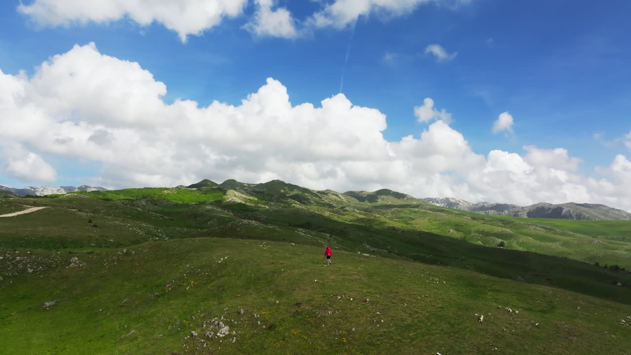 Woman in red jacket wander alone in lush green Montenegro mountains; drone