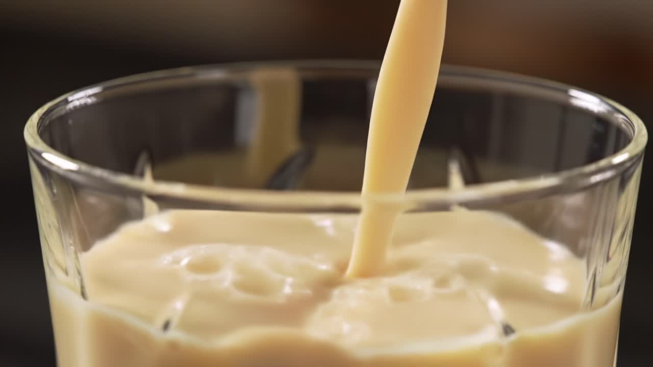Rich Creamy Drink Being Poured into a Glass: A Close-Up of the Smooth Texture and Color Transition from Pouring to Filling a Clear Crystal Glass