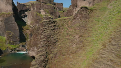 Birds-eye-of-green-hills-of-canyon-with-river-flowing-through-it-in-Iceland.-Aerial-view-flying-through-mossy-covered-hills-discovering-canyon-in-icelandic-countryside