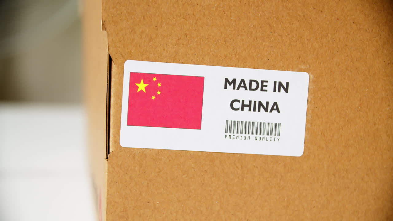 Hands applying MADE IN CHINA flag label on a shipping cardboard box with products