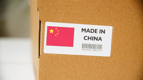 mains appliquant une étiquette de drapeau fabriqué en chine sur une boîte en carton d'expédition avec des produits