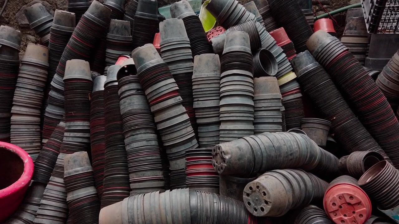 Vista di vasi da vivaio in plastica impilati e forniture da giardinaggio conservati in un'area di lavoro orticola con contenitori per tubi e attrezzature preparati per la coltivazione e la manutenzione delle piante.