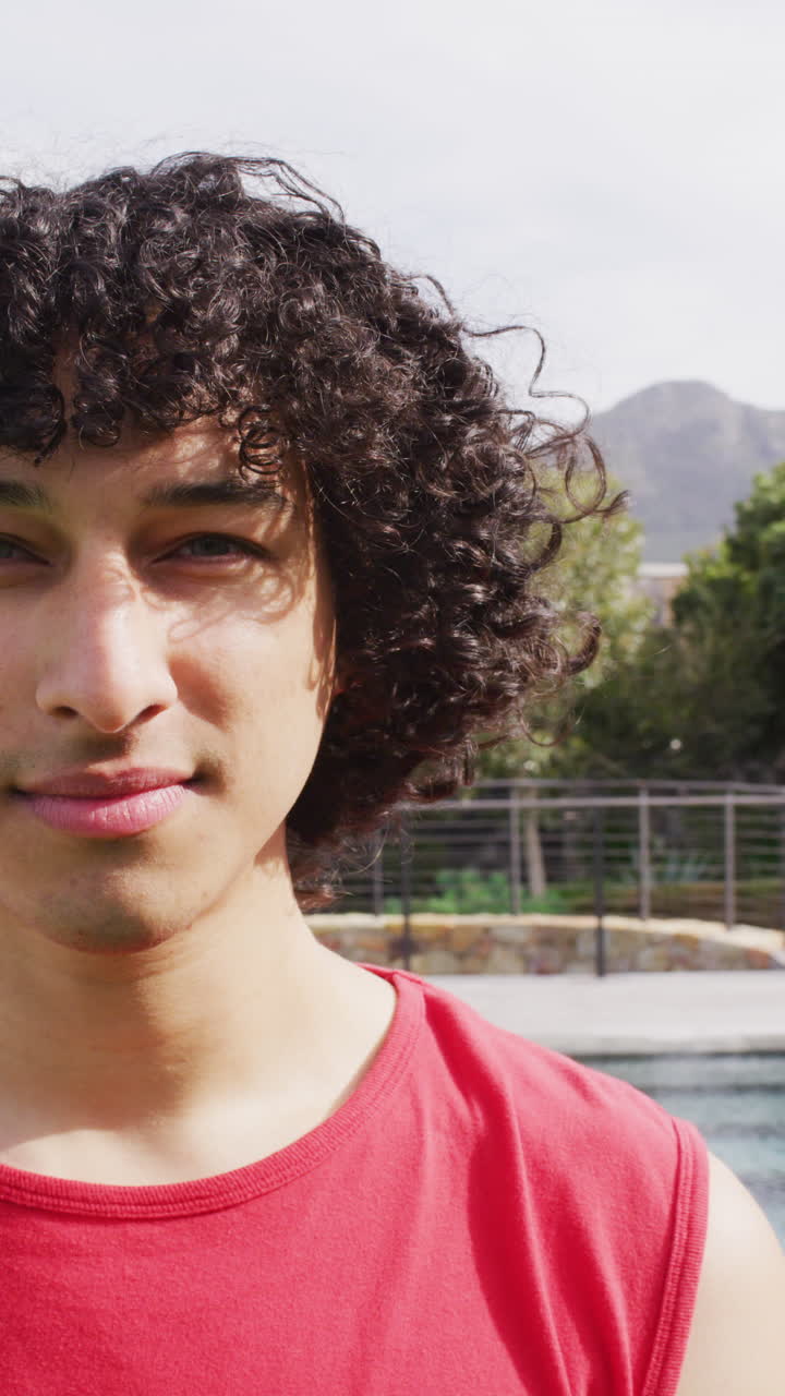 vídeo vertical en primer plano retrato de un hombre biracial sonriendo a la cámara al aire libre en el jardín