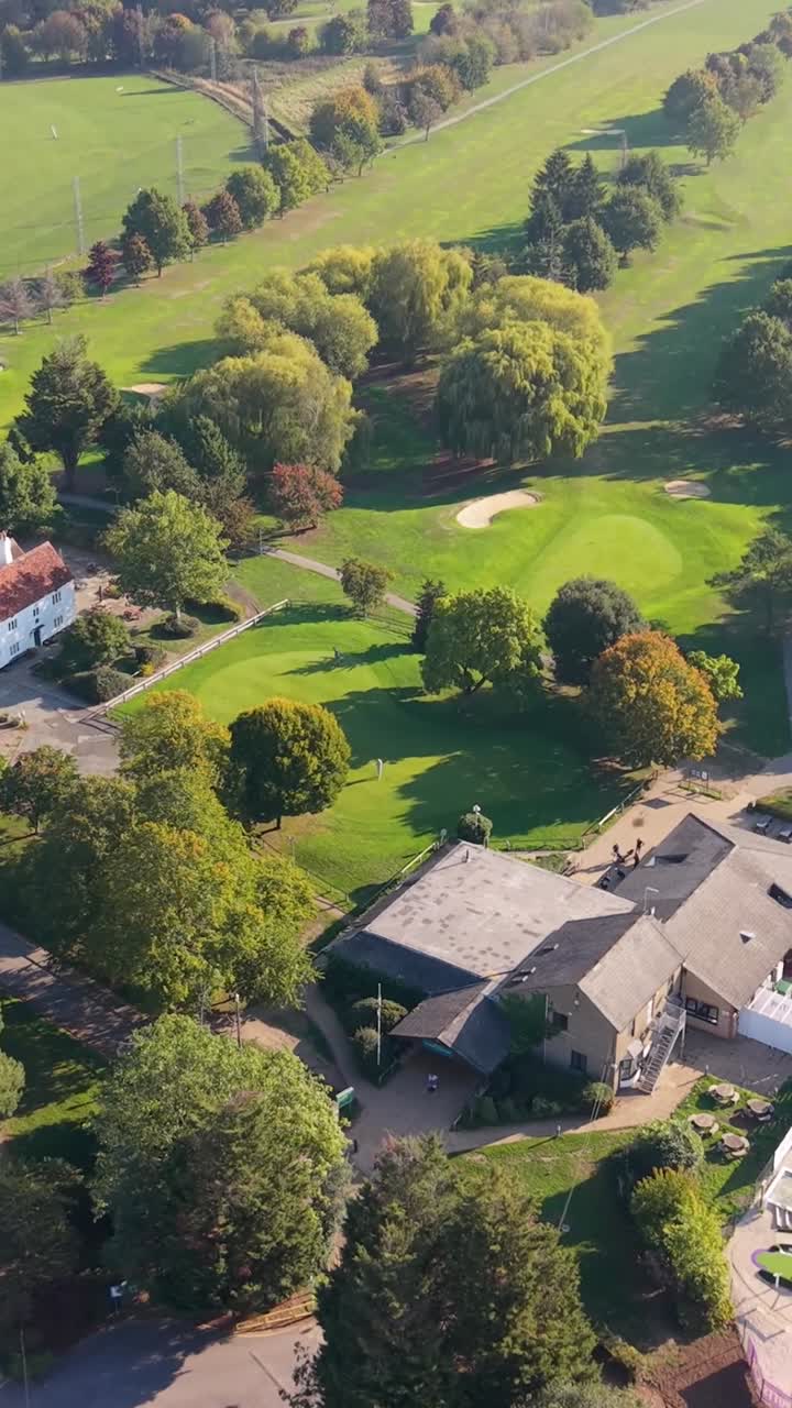 Vertical format aerial drone rise over Cheshunt Golf Course, Hertfordshire, England. Camera tilts down to reveal the clubhouse, 18-hole mini golf course, and several fairways