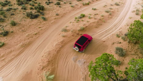 drone following a red jeep wrangler running in slow motion through sandy landscape towards white pocket in utah, usa