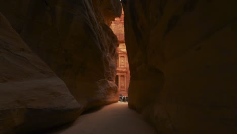 walking toward the treasury through the siq at petra, historic unesco heritage site carved into sandstone in jordan. famous indiana jones last crusade filming location and tourist destination khaznet. revealing shot.