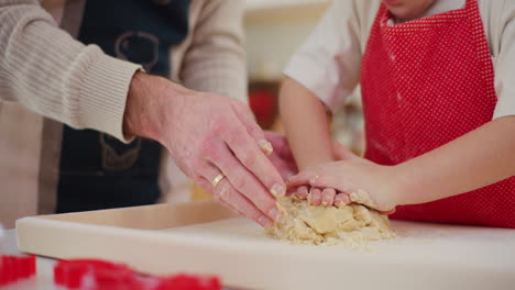 dad helps boy knead bread dough by hand in the kitchen