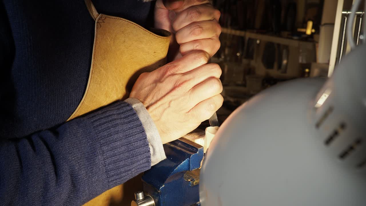 Primo piano di un artigiano che utilizza una sgorbia per intagliare il legno in un laboratorio ben illuminato, con le mani che impugnano lo strumento con precisione controllata