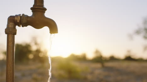 Frau-Wäscht-Sich-Bei-Sonnenaufgang-Auf-Ländlichem-Ackerland-Die-Hände-Unter-Leitungswasser-Mit-Frischem-Wasser