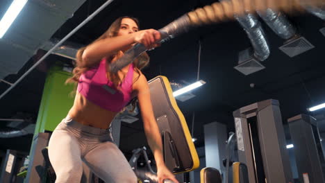 woman with battle ropes exercise in the fitness gym. young female wearing sportswear. beautiful body.