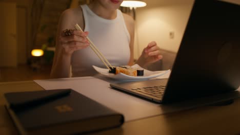 woman eating sushi while working on laptop at night