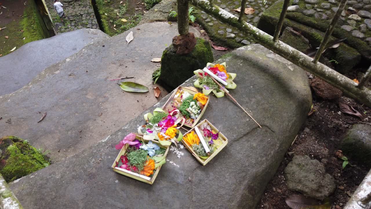 ofrendas de flores balinesas para los espíritus en el templo antiguo de goa garba, regalo colorido para la oración religiosa, cigarrillos y hojas de coco, hecho a mano, bali, indonesia