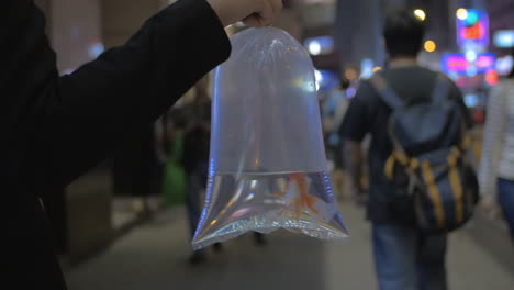 cámara lenta en hong kong china en una calle ocupada chica sosteniendo una bolsa transparente con agua y pez dorado