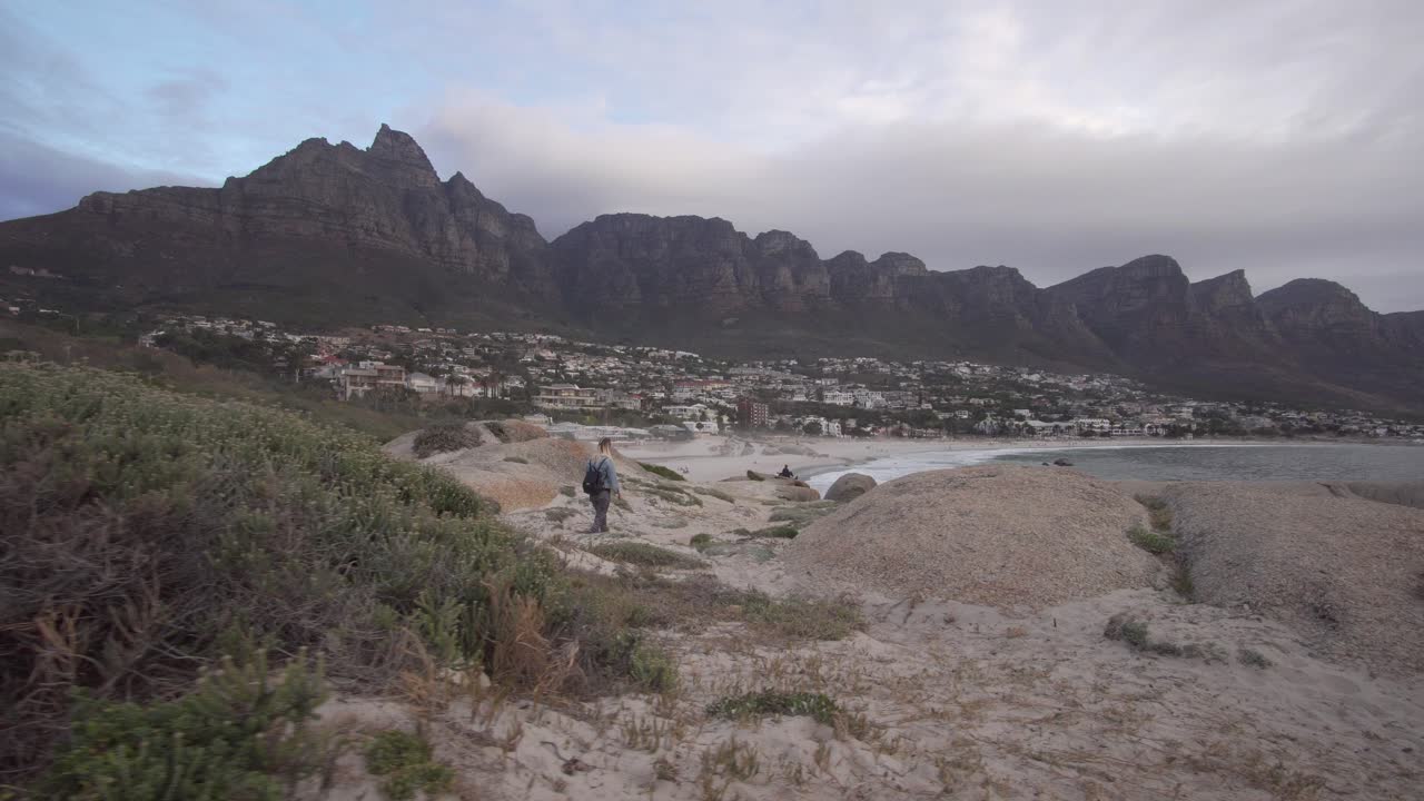 Blonde Woman walks on the sand with Table Mountain and Camps Bay in the background in Cape Town, South Africa