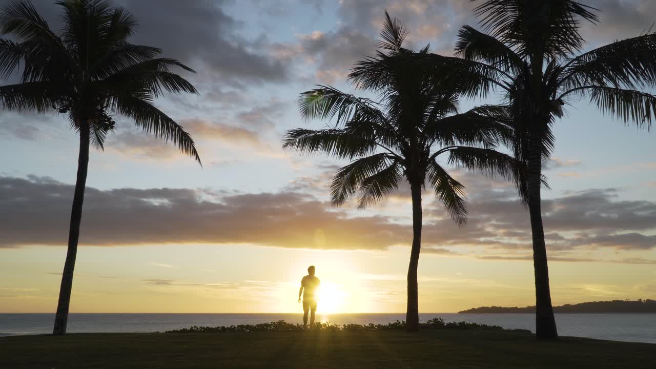 Tourist walking towards sunset on tropical shore with silhouette coconut trees
