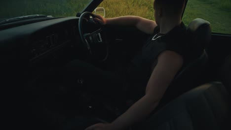man driving a vintage car in a field at sunset