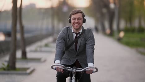 smiling young businessman on bicycle listening to music and smiling