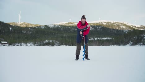 Pescador-Noruego-Está-Perforando-En-Un-Lago-Congelado-Usando-Una-Barrena-De-Hielo