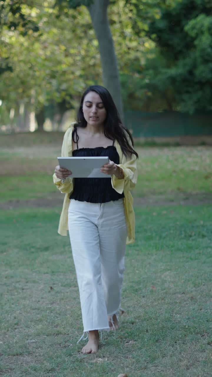 Donna con tablet che cammina a piedi nudi in un parco